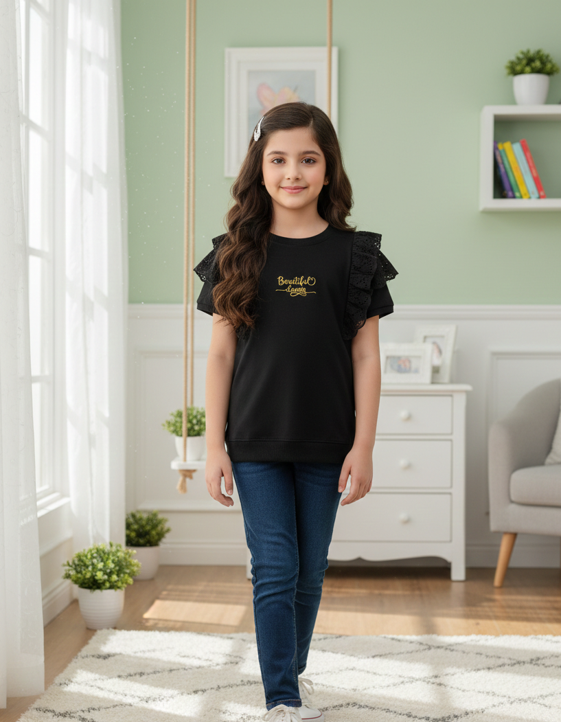 Young girl wearing a black ruffled shirt and blue jeans standing in a room with a green wall and white furniture.